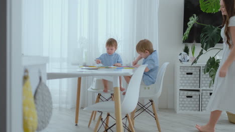 Young-Mom-and-two-sons-2-4-years-old-draw-pencils-drawing-on-boomega-sitting-at-the-living-room-table-in-slow-motion